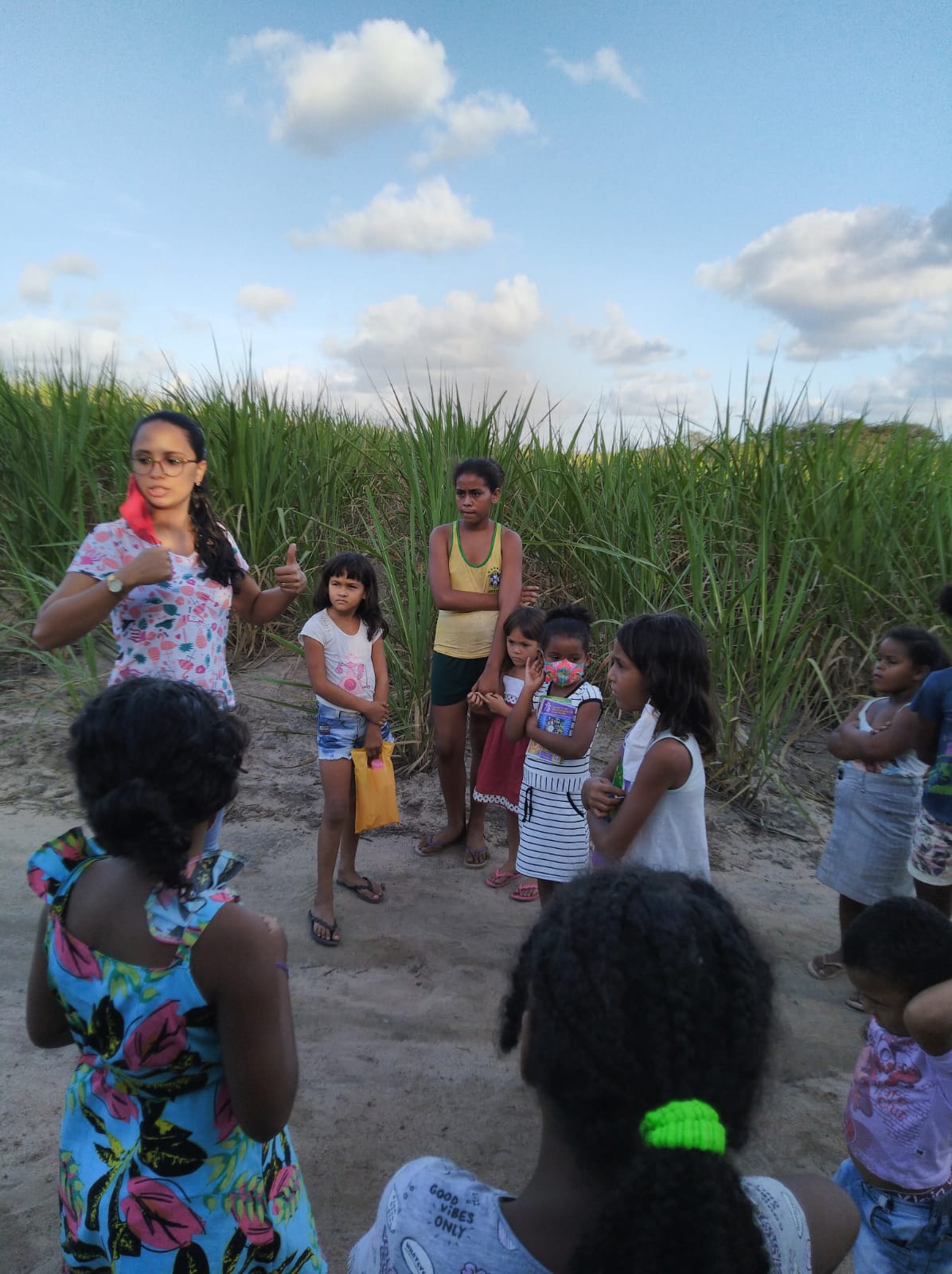 Imagem da professora Cleyse ministrando aula de educação ambiental entre a mata e um canavial